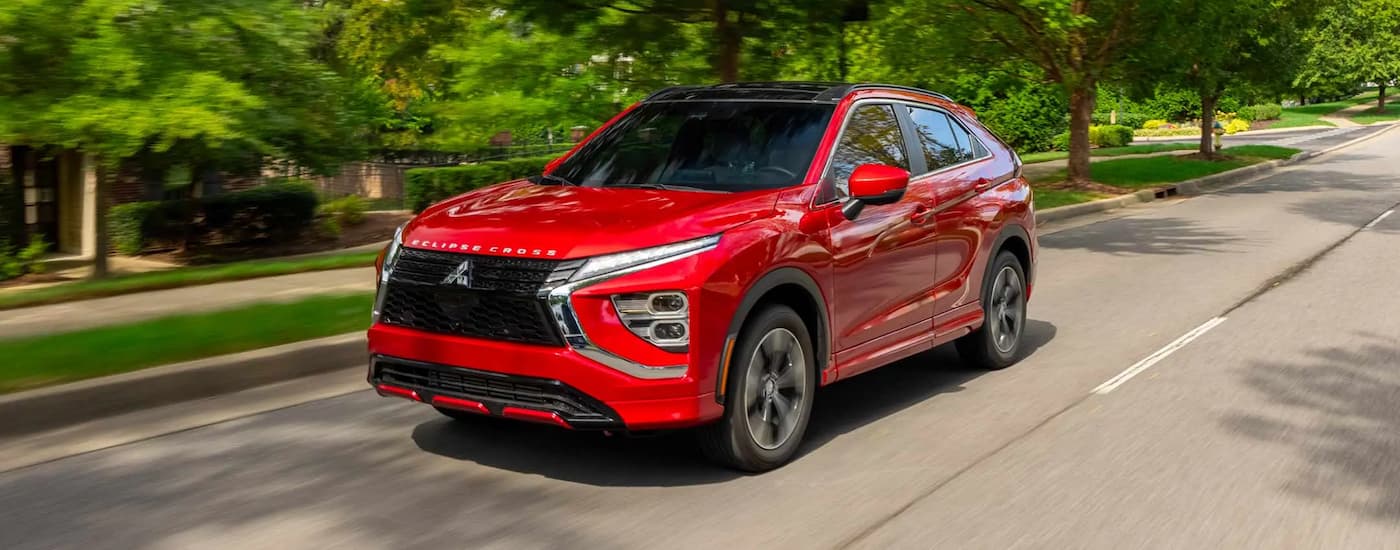 A red  2023 Mitsubishi Eclipse Cross is shown driving on a suburban street.