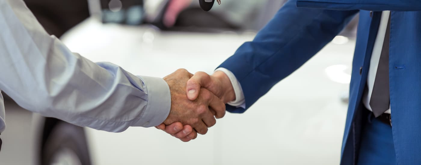 Two people are shown shaking hands at a car dealership.