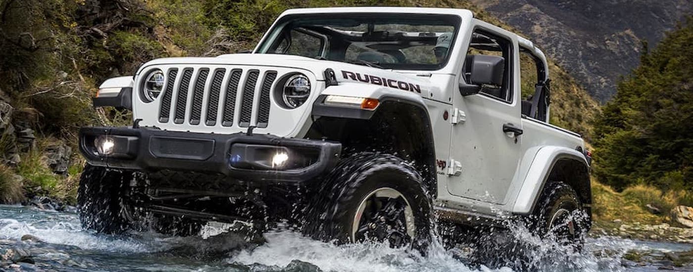 A white 2018 Jeep Wrangler Unlimited is shown from the front driving through a river.