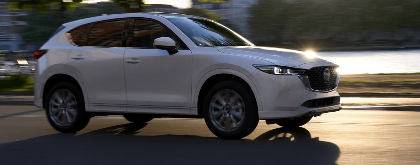A white 2022 Mazda CX-5 is shown from the side driving past a river.