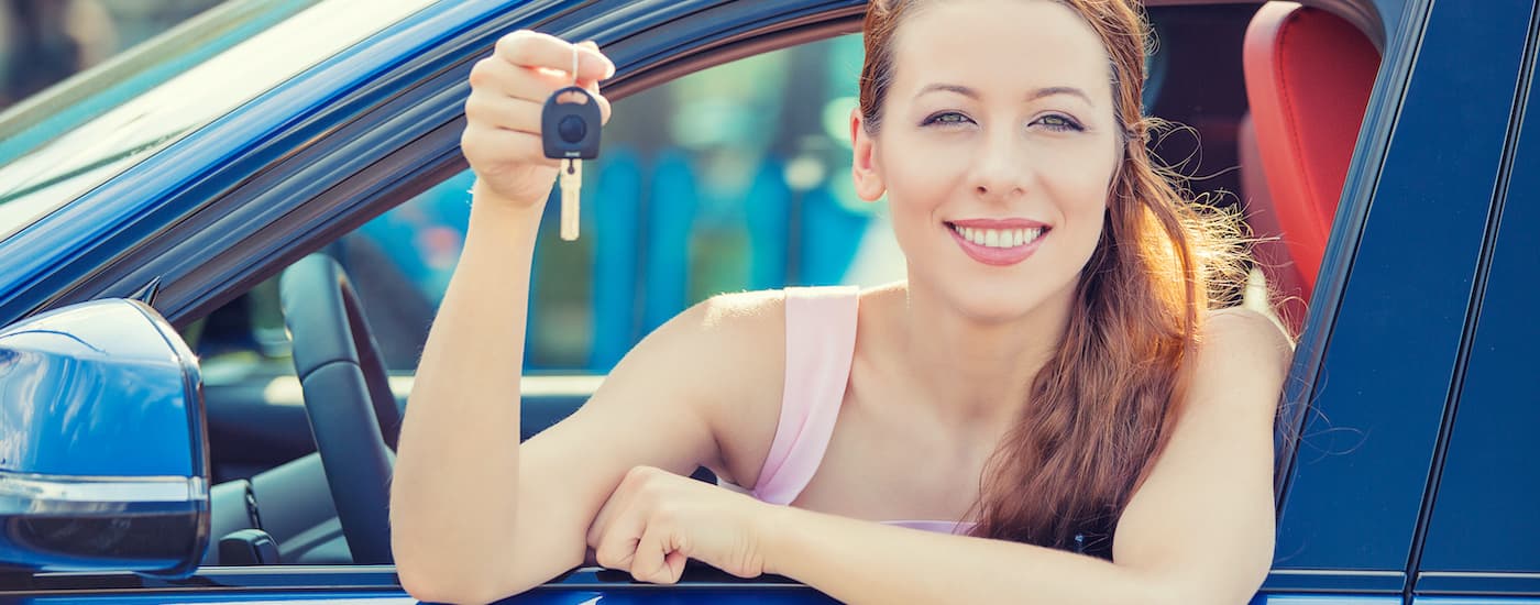 A person is shown holding a car key out the window of a car.