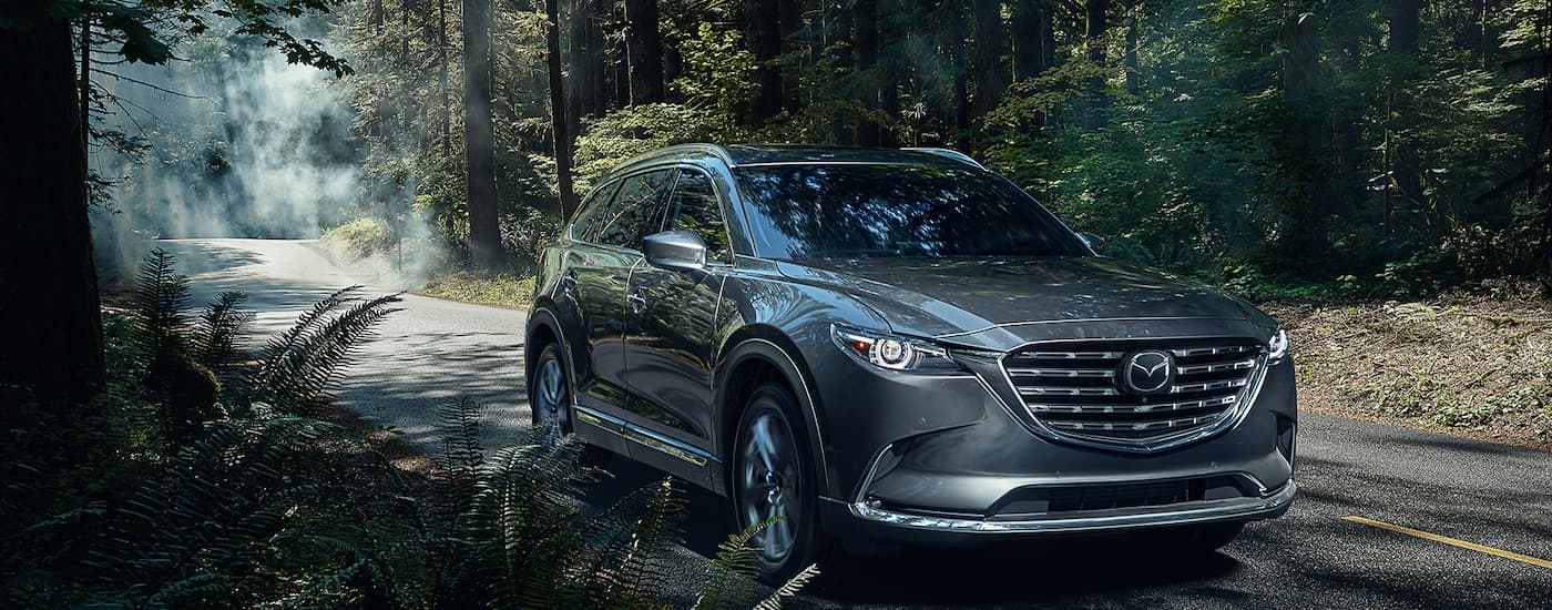 A popular SUV for sale, a grey 2022 Mazda CX-9, is shown driving through a forest.