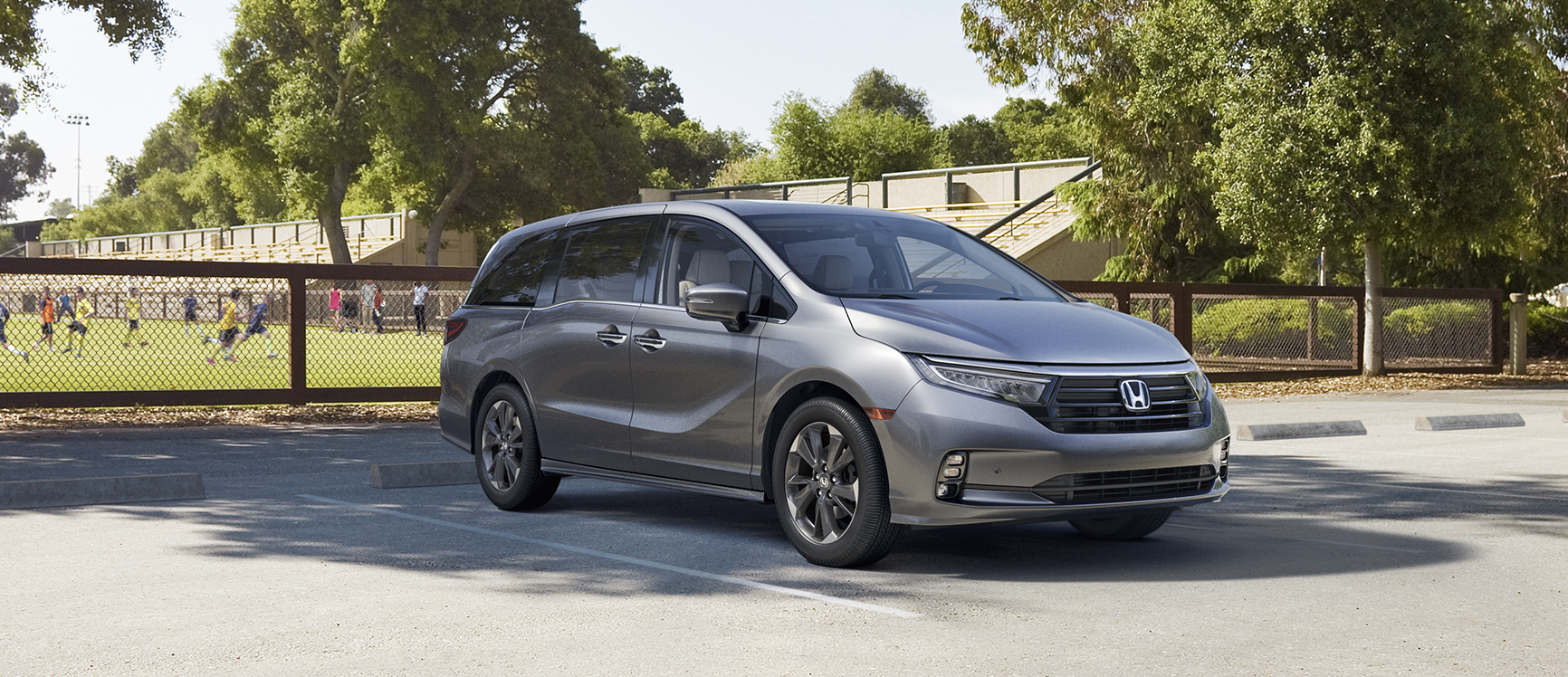 2023 Honda Odyssey Grey parked in parking lot kids playing soccer in the background 