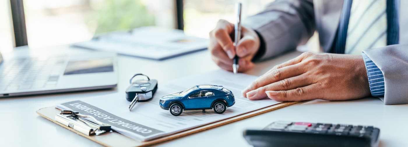 A car salesman is shown filling out credit application paperwork at a dealership.