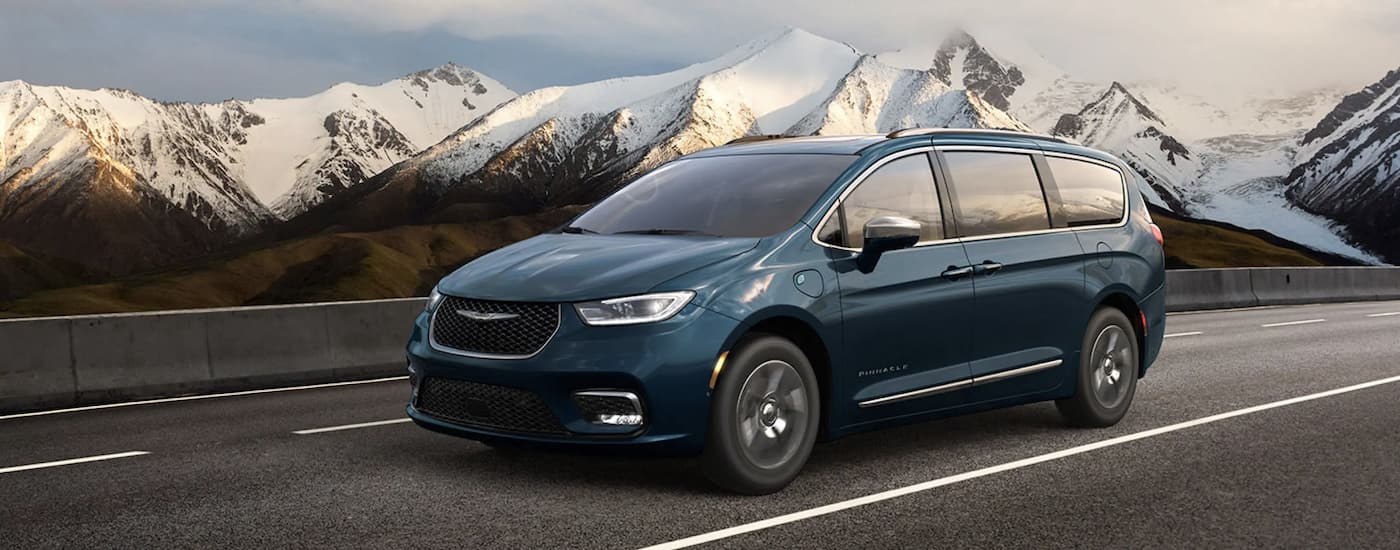 A blue 2022 Chrysler Pacifica is shown driving on an open road past mountains.