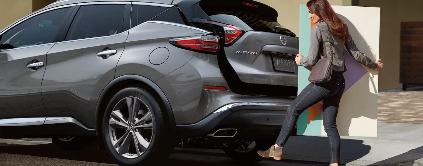 A woman is shown opening the liftgate on a grey 2022 Nissan Murano.