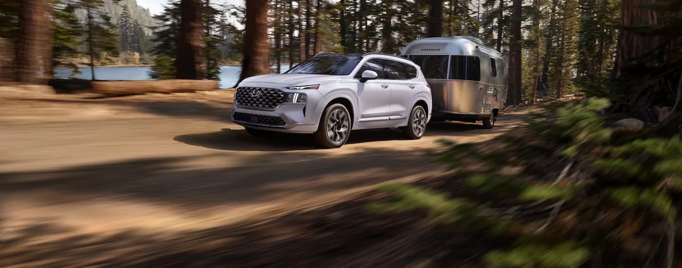 A white 2023 Hyundai Santa Fe is shown towing a silver camper.