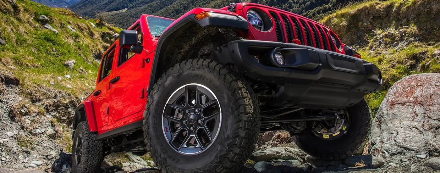 A red 2022 Jeep Wrangler is shown driving up a steep rocky trail.