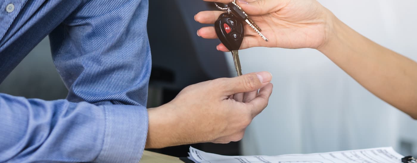 A car salesperson is shown passing a car key.