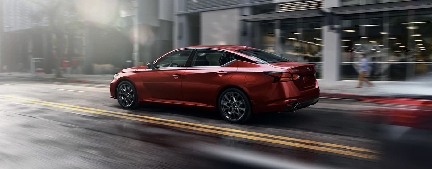A red 2023 Nissan Altima is shown from the side driving through a city after leaving a Nissan dealer in Edmonton.