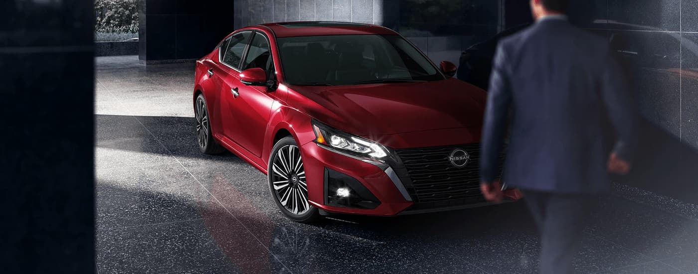 A man is shown walking towards a red 2023 Nissan Altima SL after leaving a Nissan dealer near you.