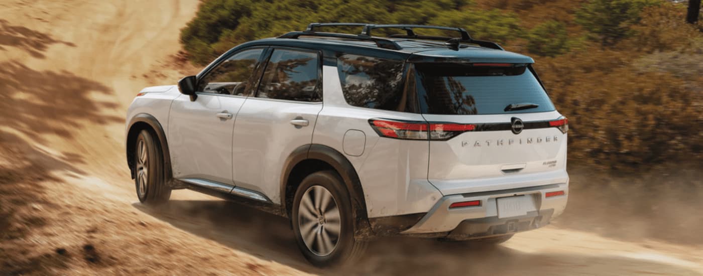 A red 2023 Nissan Pathfinder Platinum is shown from a rear angle while driving on a dirt road.