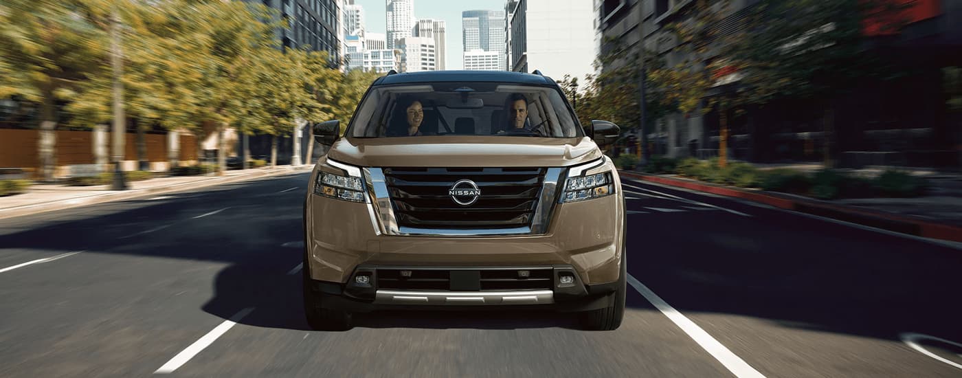 A brown 2023 Nissan Pathfinder is shown from the front driving on a city street.