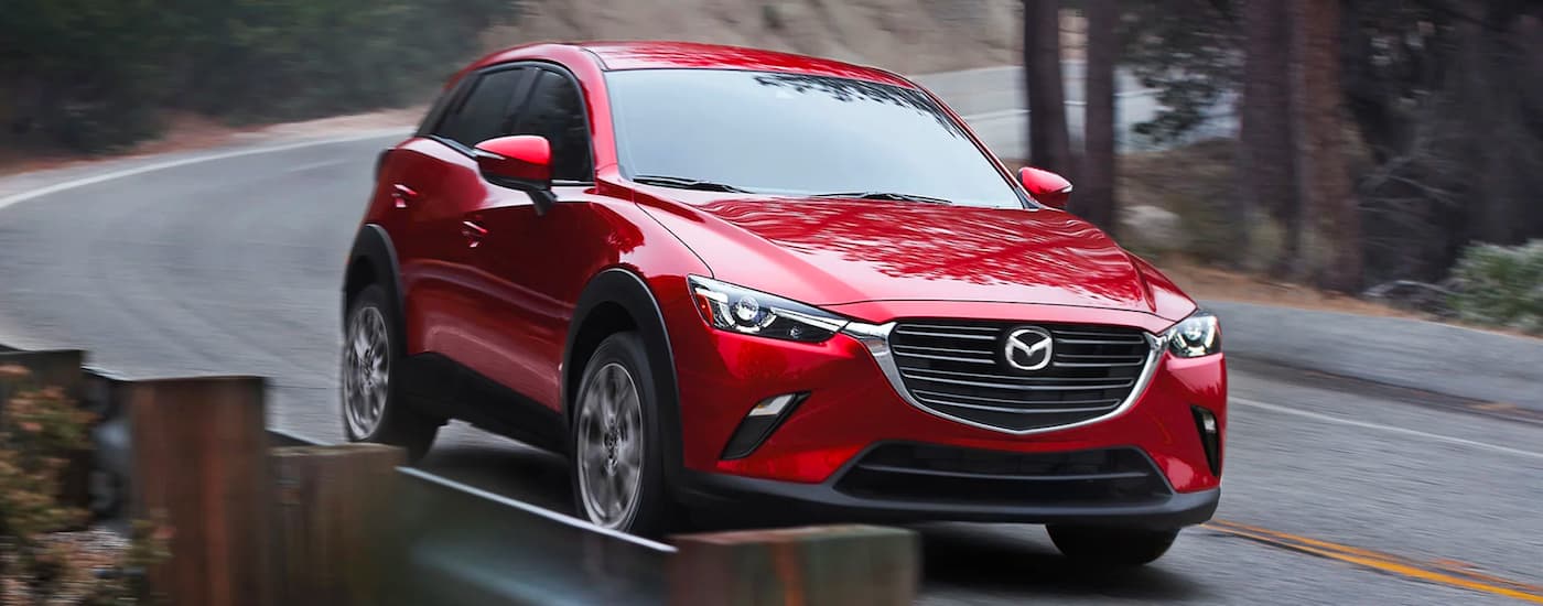A red 2020 Mazda CX-3 is shown driving on a tree-lined road.