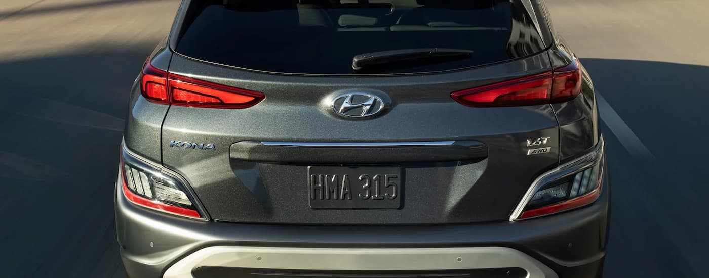 A grey 2022 used Hyundai Kona for sale is shown from the rear driving on a highway.