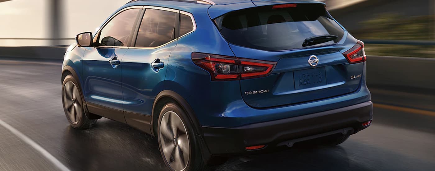 A blue 2021 used Nissan Qashqai for sale is shown from the rear driving on an open highway.