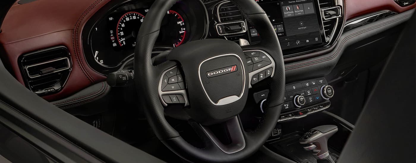A close up of the black and red interior of a 2022 Dodge Durango shows the steering wheel and center console.