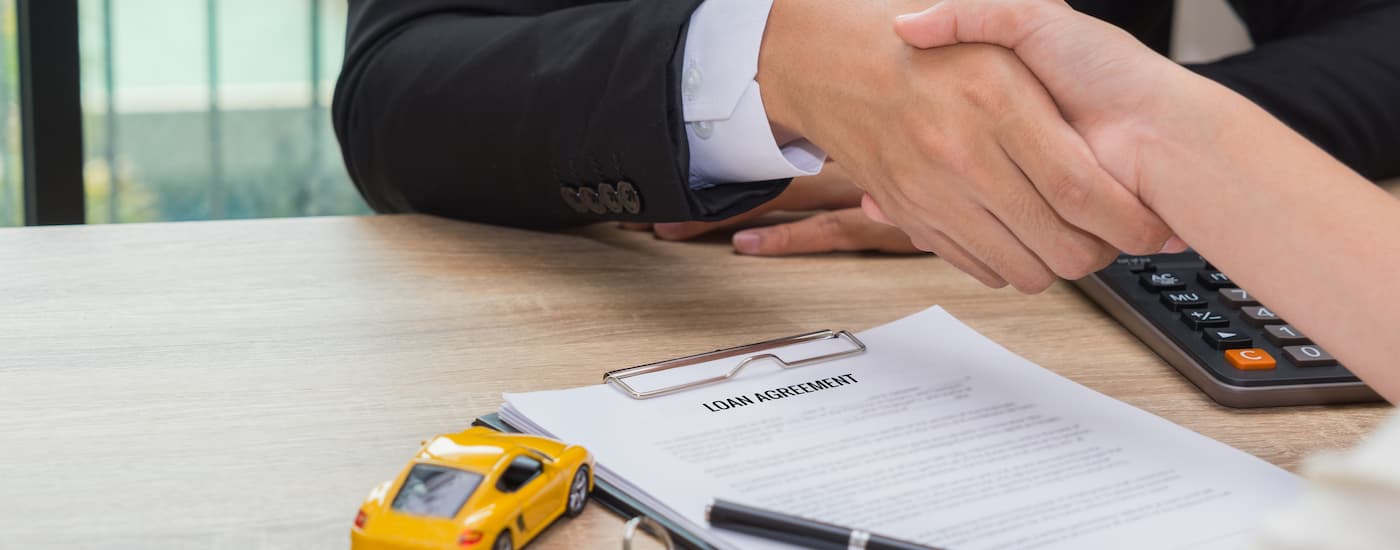 A close up of a salesman shaking hands with a customer over a clipboard is shown.