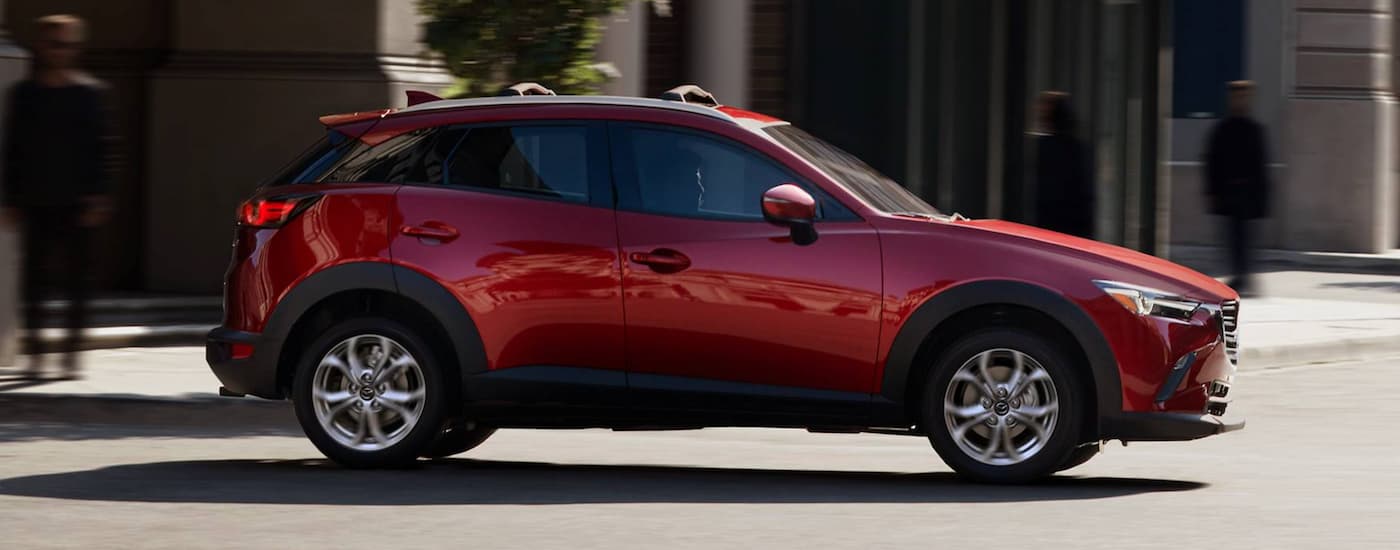 A red 2021 Mazda CX-3 is shown from the side driving on a city street.