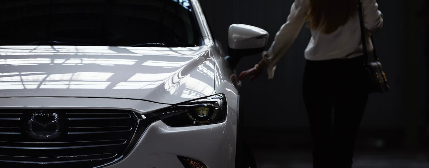 A woman is shown opening the door of a white used 2018 Mazda CX-3 for sale.