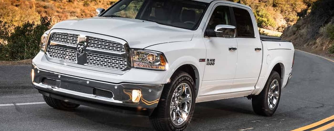 A white 2013 used Ram 1500 for sale is shown driving up a winding road.