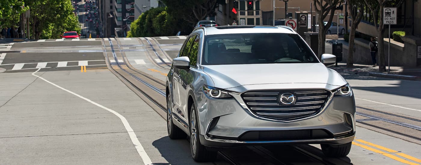 A silver 2018 Mazda CX-9 is shown driving on a city street.