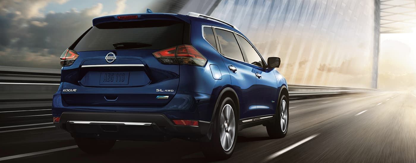 A blue 2017 Nissan Rogue SL is shown from the rear driving on a bridge.