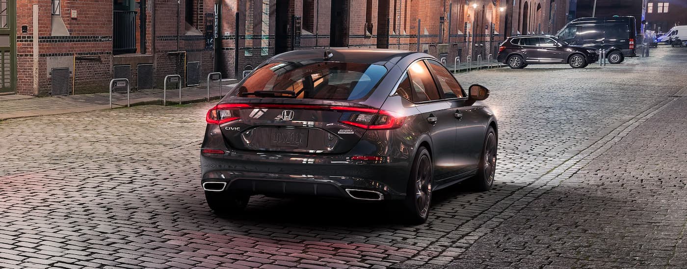 A grey 2023 Honda Civic Sport Touring driving on a cobblestone street at night