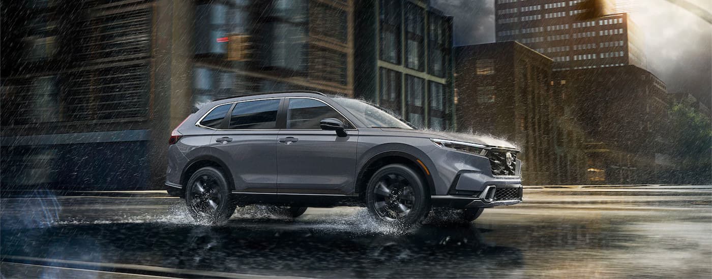 A grey 2023 Honda CR-V Hybrid Sport Touring driving on a city street in the rain