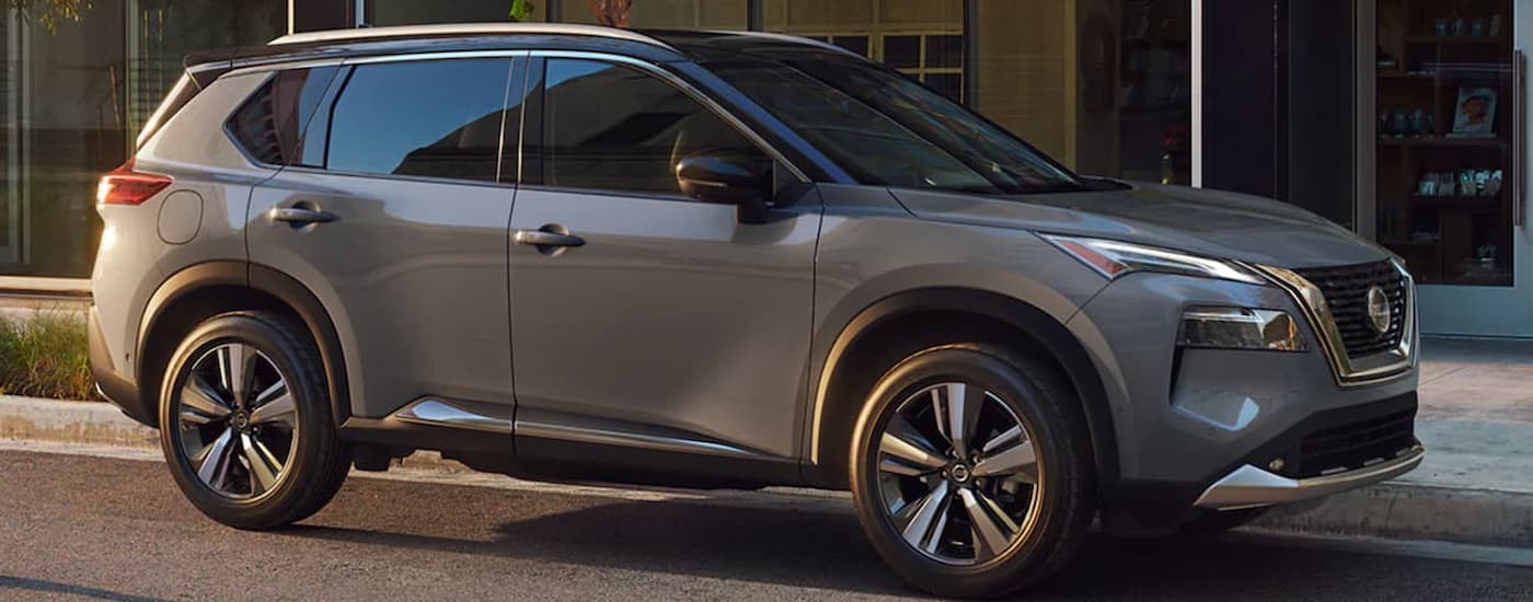A grey 2021 Nissan Rogue is shown from the side while parked on a city street.