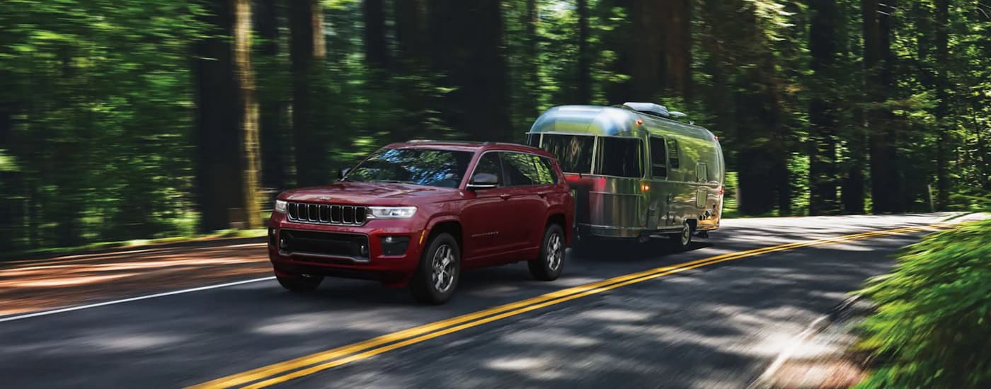 A red 2022 Jeep Grand Cherokee for sale is shown towing a silver trailer on a forest road.