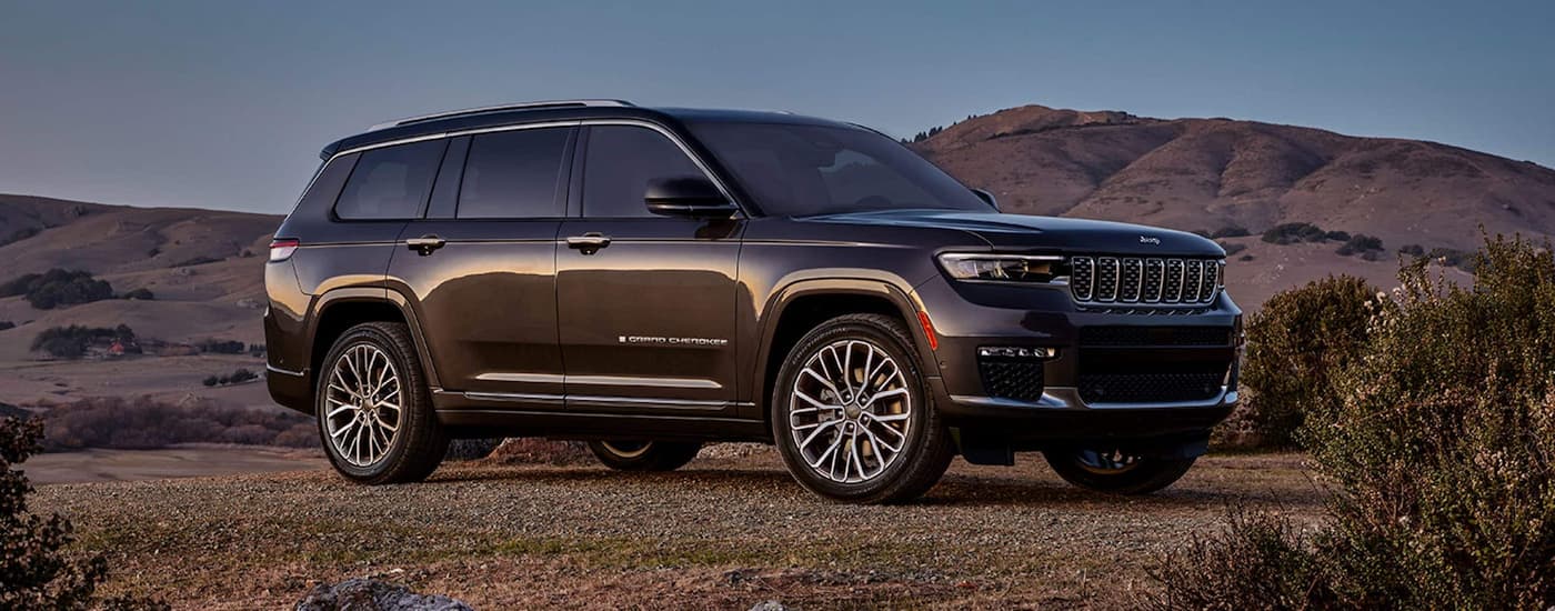 A black 2023 Jeep Grand Cherokee is shown parked in a remote area with mountains in the distance.