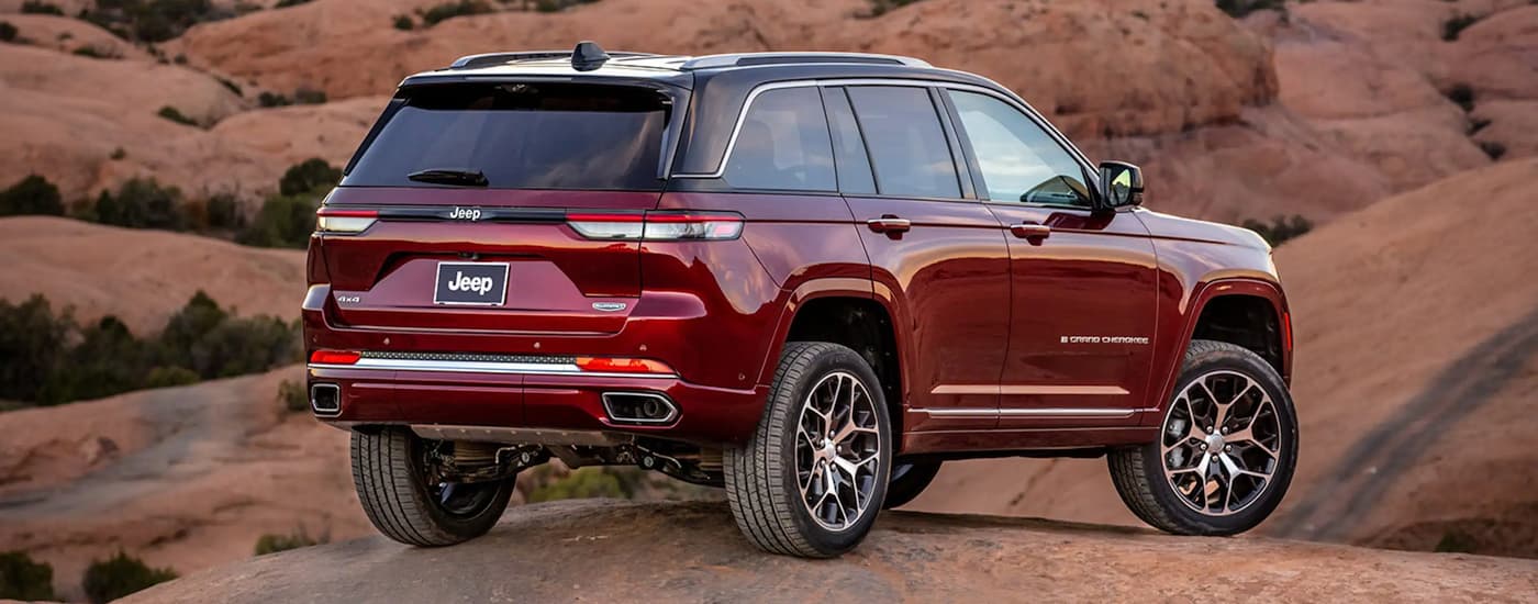 A red 2023 Jeep Grand Cherokee for sale is shown from a rear angle while parked on a brown rocks.
