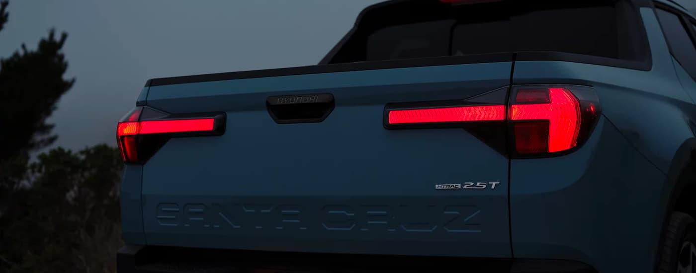 A light blue 2023 Hyundai Santa Cruz is shown from the rear with illuminated taillights.