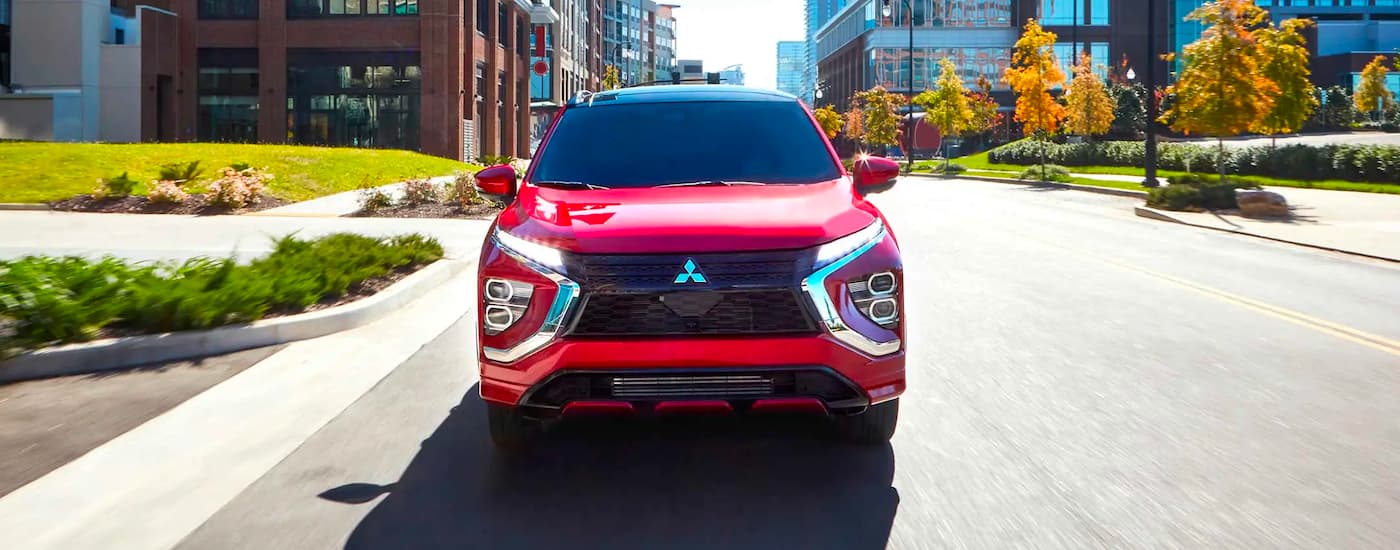 A red 2023 Mitsubishi Eclipse Cross for sale is shown from the front driving on a city street.