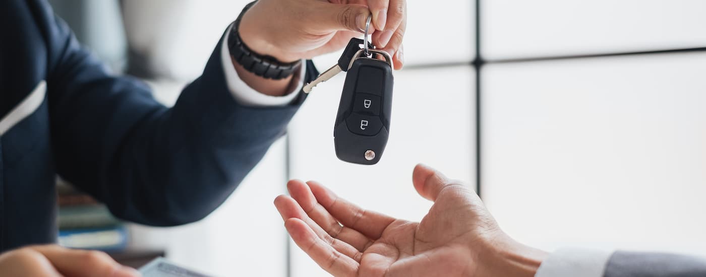 A car salesman is shown handing a car key to a customer after talking about subprime loans.
