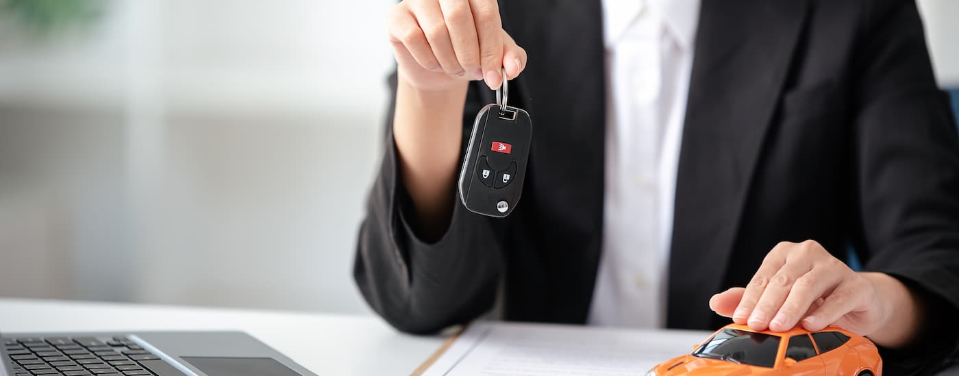 A car salesman is shown holding a car key while sitting at a desk.