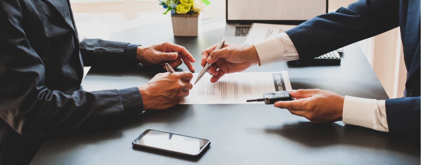 A salesman is shown going over paperwork with a customer trying to sell their car.