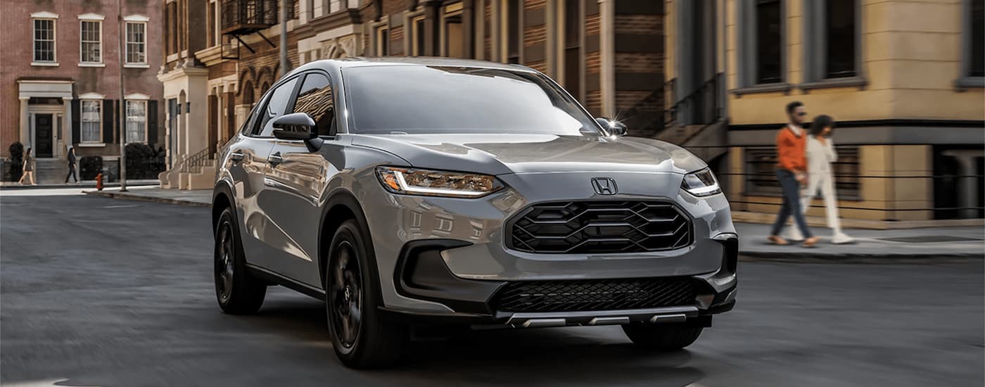 A grey 2023 Honda HR-V Sport driving on a wide city street.