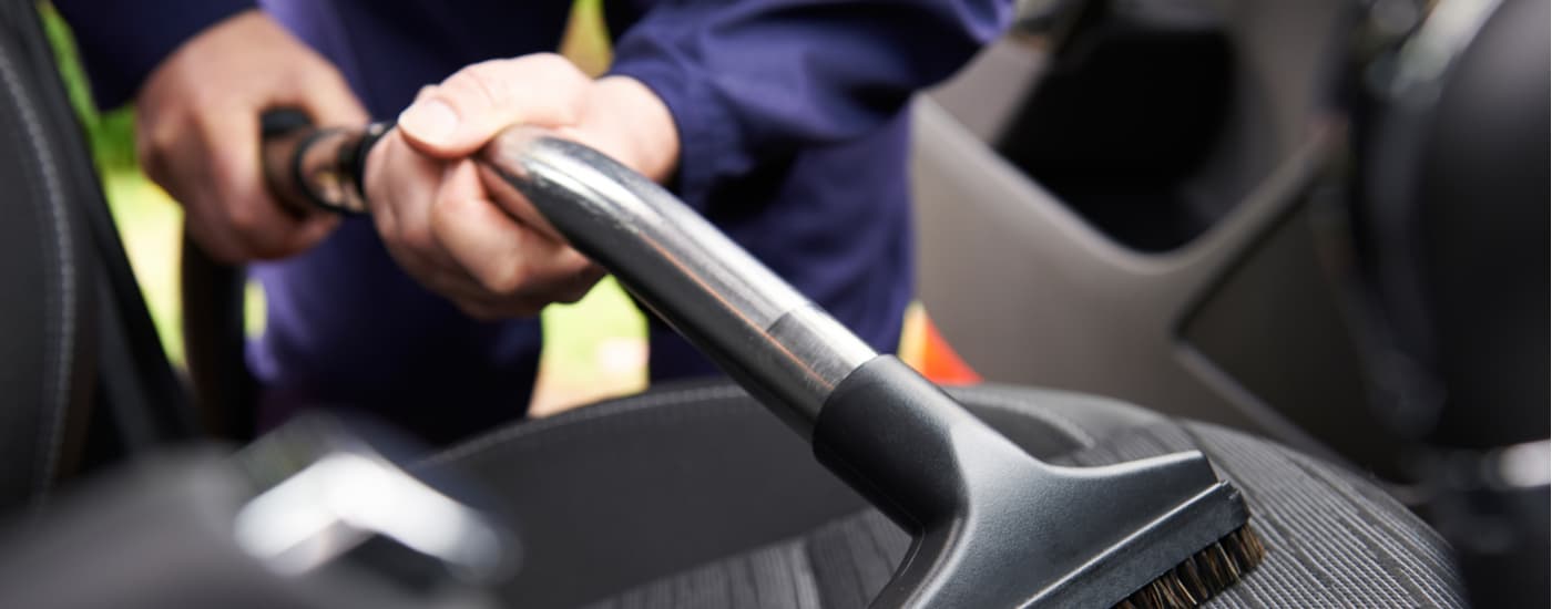 A person is shown using a vacuum to clean the interior of their vehicle.