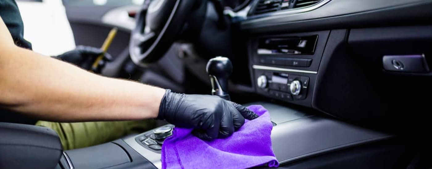 A hand is shown using a purple rag to clean the center console of their vehicle.