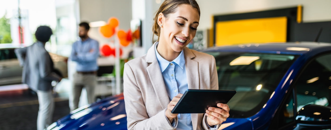 A salesperson is shown holding a tablet and talking to a customer who searched "sell my car."