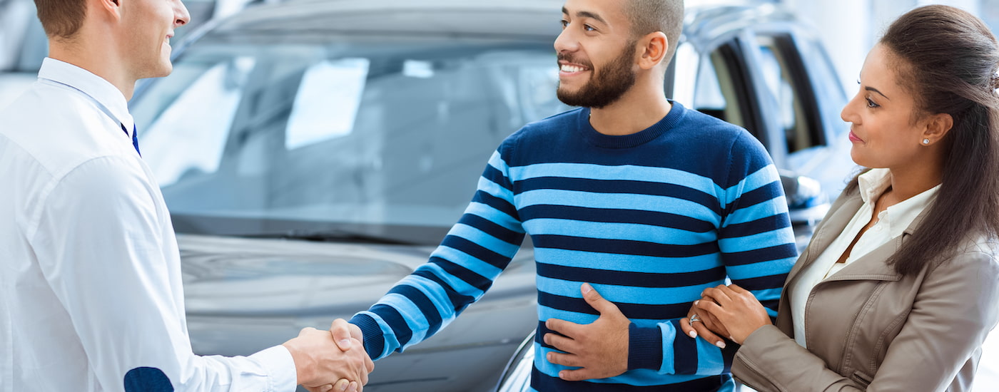 A couple is shown talking to a salesperson at a car dealership.