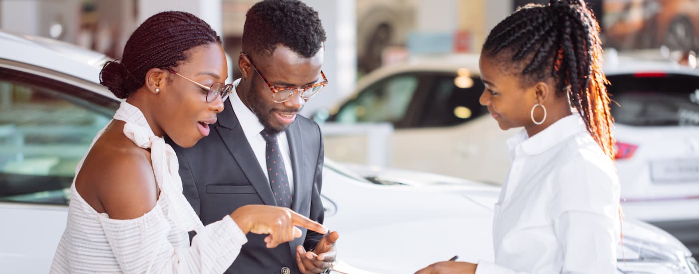 A couple is shown talking to a salesperson at a dealership after searching "sell my car."