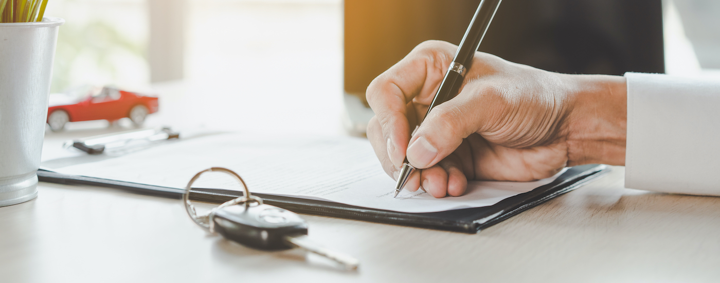A person is shown signing paperwork next to a key and a toy car.