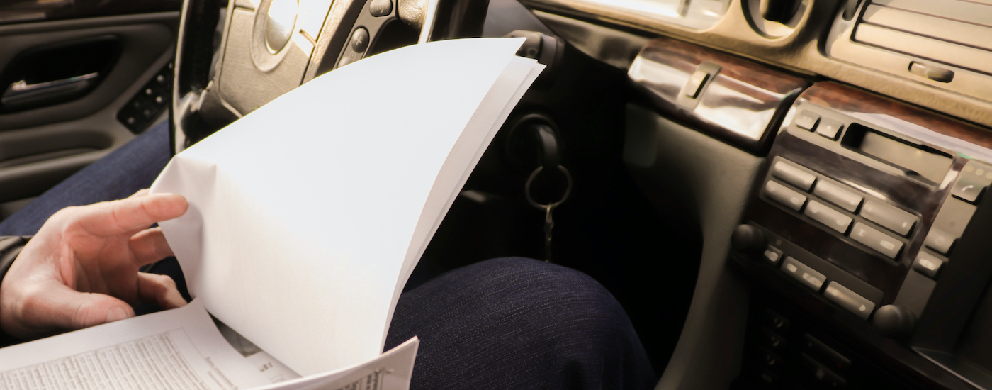 A person is shown looking at paperwork in the front seat of a vehicle.