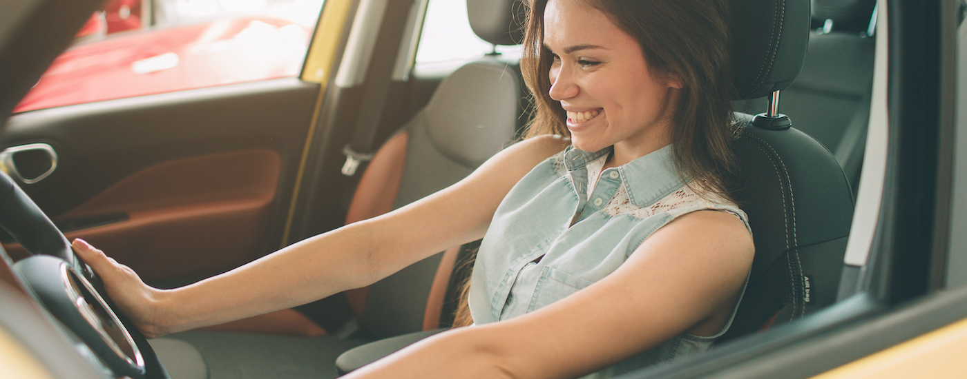 A person is shown sitting in the front seat of a vehicle and smiling.