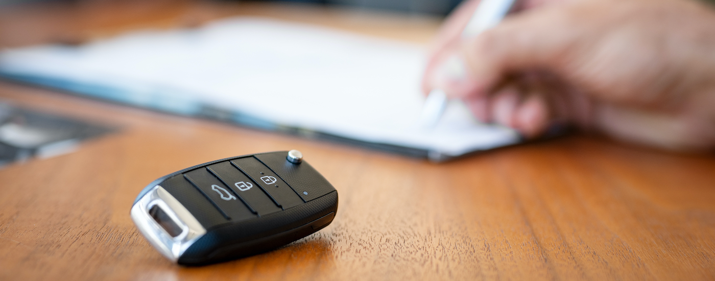 A person is shown filling out paperwork next to a car key.
