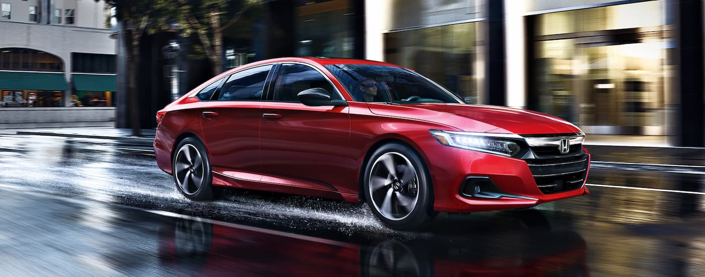 A red 2022 Honda Accord Sport drives on wet city streets after visiting a certified pre-owned Honda dealer.