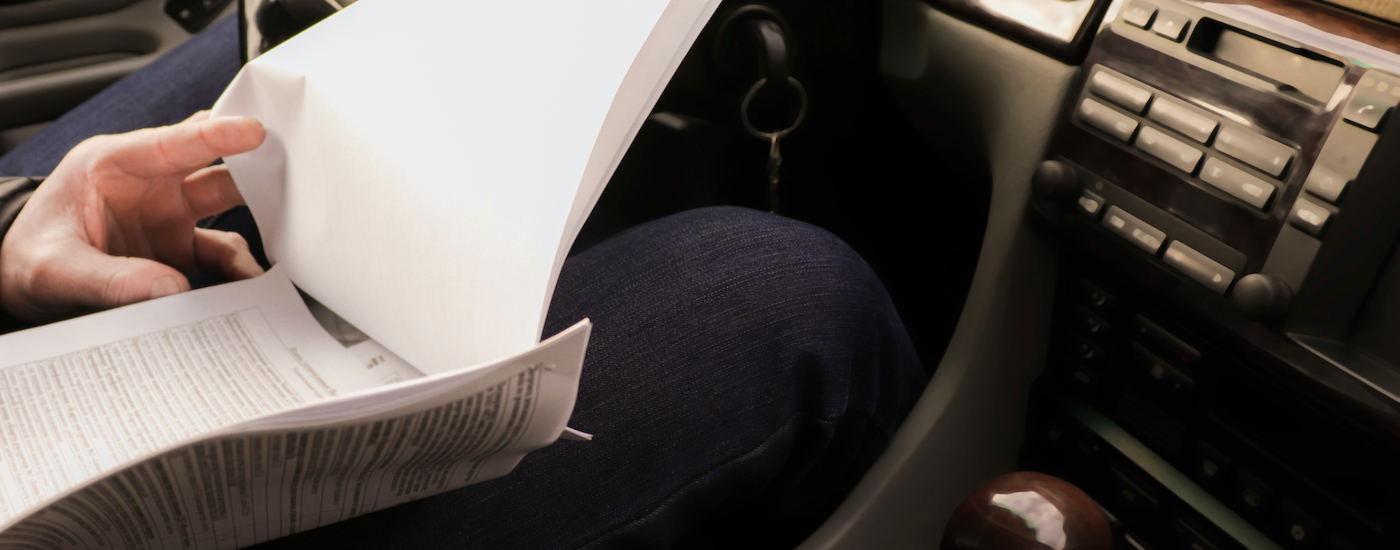 A person is shown looking at paperwork in their car after searching "sell my car."